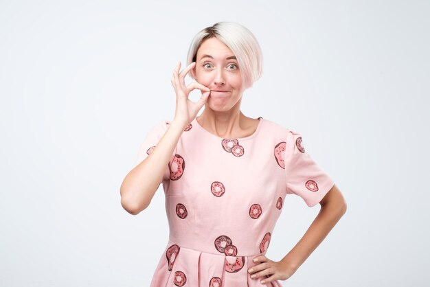 Kaukasische mooie vrouw met kort geverfd haar die haar mond dicht ritst