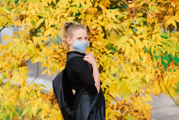 Kaukasische schoolmeisje tiener met een medisch masker dat het gezicht beschermt op de achtergrond van een herfstlandschap