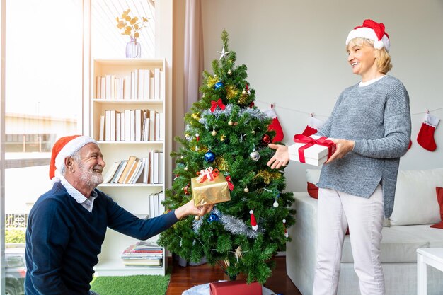 Kaukasische senior oudere man geeft geschenkdoos aan vrouw terwijl hij samen de kerstboom versiert voor het festival