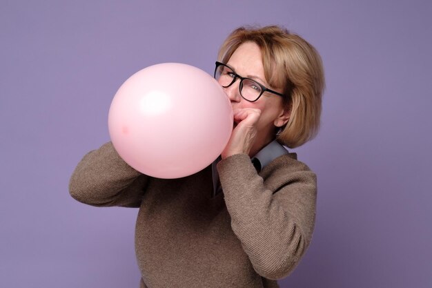 Kaukasische senior vrouw blaast roze ballon Bereid je voor op verjaardagsfeestje