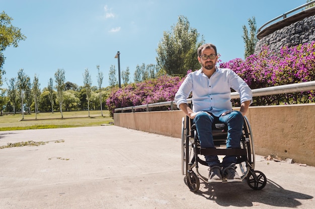 Kaukasische Spaanse Latino volwassen mannelijke zakenman in een rolstoel in een straatpark met kopieerruimte, met de lucht, bomen en een rozentuin achter hem op de achtergrond