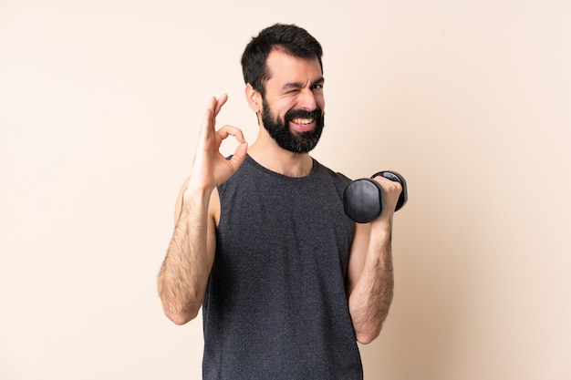 Kaukasische sportmens die met baard gewichtheffen over geïsoleerd maken die ok teken met vingers tonen