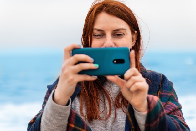 Kaukasische toeristische vrouw maakt foto's op de telefoon in de buurt van de oceaan