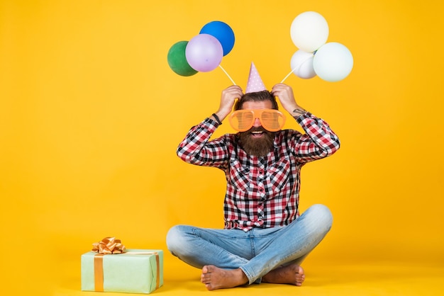 Kaukasische volwassen hipster met grappige feestbril in geruit hemd met ballonnen en geschenkdoosverjaardag