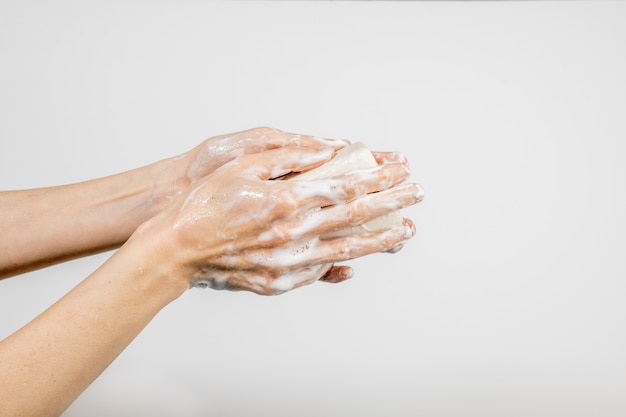 Kaukasische vrouw die haar handen met bruisende zeepstaaf wast die op witte muur wordt geïsoleerd