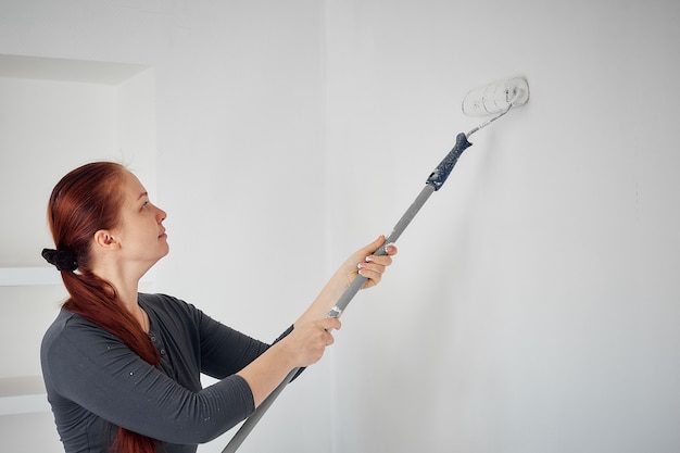 Kaukasische vrouw die met een rol de muren in de flat schildert.