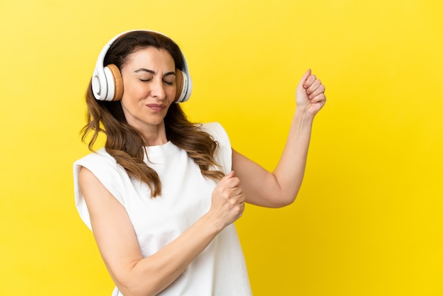 Kaukasische vrouw van middelbare leeftijd geïsoleerd op gele achtergrond muziek luisteren en dansen