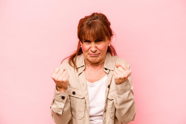 Kaukasische vrouw van middelbare leeftijd geïsoleerd op roze achtergrond boos schreeuwen met gespannen handen