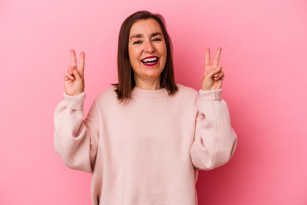 Kaukasische vrouw van middelbare leeftijd geïsoleerd op roze achtergrond met overwinningsteken en breed lachend.