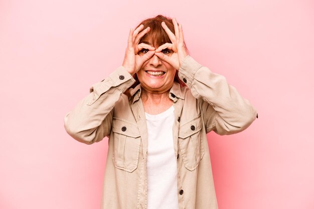 Kaukasische vrouw van middelbare leeftijd geïsoleerd op roze achtergrond opgewonden houden ok gebaar in de gaten