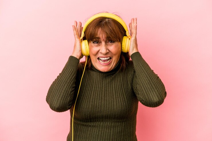 Foto kaukasische vrouw van middelbare leeftijd luisteren naar muziek geïsoleerd op roze achtergrond die oren bedekt met handen.