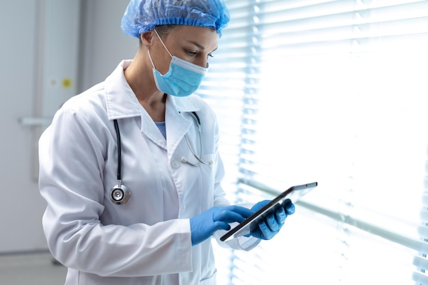 Kaukasische vrouwelijke arts die masker en latexhandschoenen draagt die tablet gebruiken