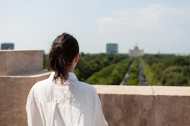 Kaukasische vrouwelijke tourit die op het dak van de toren staat en geniet van een panoramisch uitzicht op de metropool tijdens de zomervakantie. Landschap met stedelijke gebouwen vanaf observatiepunt