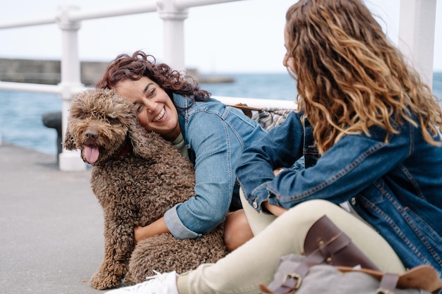 Kaukasische vrouwen die bruine waterhond kussen. Horizontale weergave van vrienden die met huisdier reizen. Levensstijl met dieren buitenshuis.