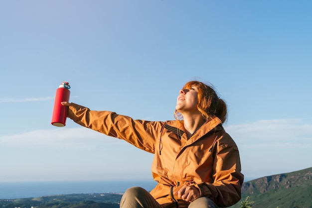 Foto kaukasische wandelaar staat op de top van een berg met een fles water en kijkt naar de lucht