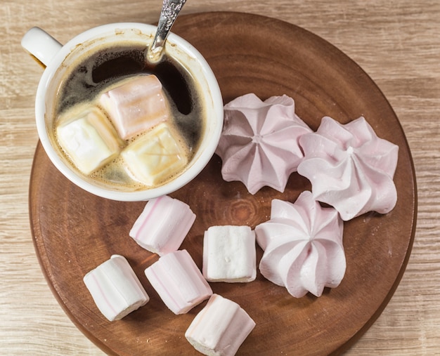 Kauwen marshmallows, meringue en kopje koffie op een houten bord