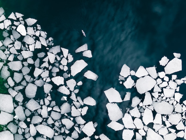 Kayak sailing between ice floes on Baikal lake in spring. Aerial drone view. Baikal lake, Siberia, Russia