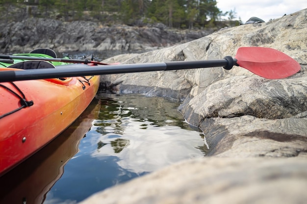 Kayaks with oars are parked against the stony shore of the lake