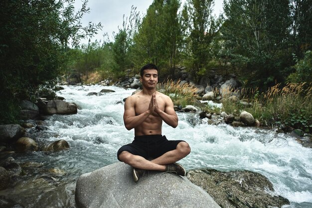 Kazachse gespierde atleet man traint en oefent door de rivier in de natuur. Aziatische knapperd doet extreme fitnesstraining buitenshuis