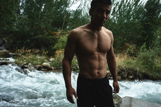 Kazachse gespierde atleet man traint en oefent door de rivier in de natuur. Aziatische knapperd doet extreme fitnesstraining buitenshuis