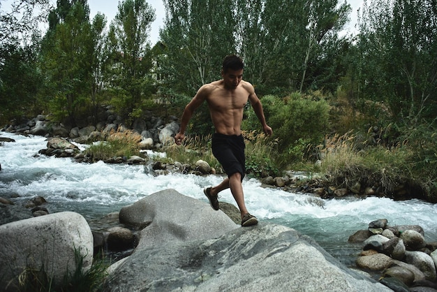 Kazachse gespierde atleet man traint en oefent door de rivier in de natuur. Aziatische knapperd doet extreme fitnesstraining buitenshuis