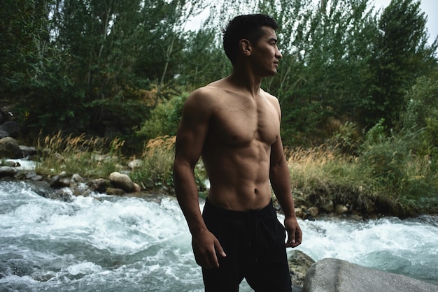 Kazakh muscular athlete man trains and exercises by the river in nature. Asian handsome does extreme fitness workout outdoors