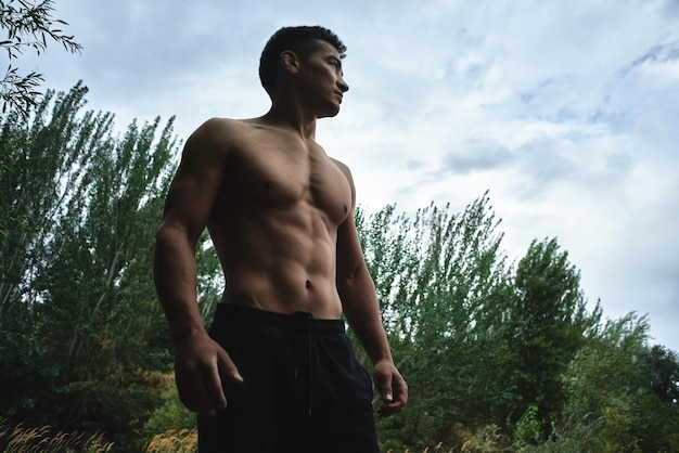 Kazakh muscular athlete man trains and exercises by the river in nature. Asian handsome does extreme fitness workout outdoors