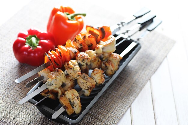 Kebab cooked on metal skewers with vegetables served on white table