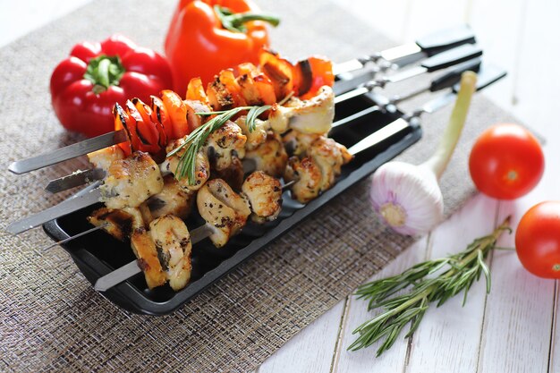 Kebab cooked on metal skewers with vegetables served on white table