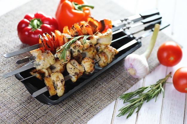 Kebab cooked on metal skewers with vegetables served on white table