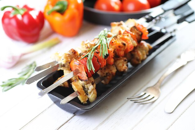 Photo kebab cooked on metal skewers with vegetables served on white table