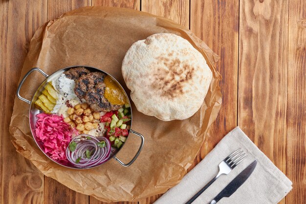 Kebab in a frying pan, pita, wooden background