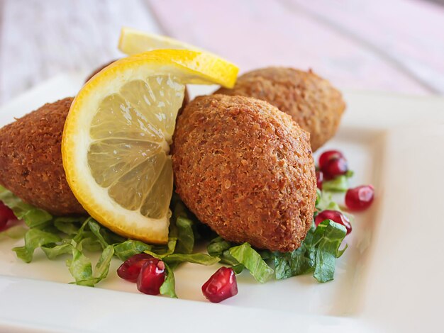 Foto kebbah kibbeh kibbe o kubbeh con fetta di limone e semi di melograno in primo piano servito in un piatto isolato sul tavolo vista laterale del fast food arabo