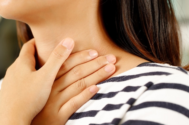 Keelpijn. Close-up van jonge vrouw ziek met haar ontstoken keel met handen om de zieke nek in blauw shirt op grijze achtergrond aan te raken. Medisch en gezondheidszorgconcept. Focus rood op om pijn te tonen.