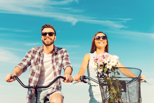 Keep calm and ride on. Low angle view of cheerful young couple smiling and riding on bicycles