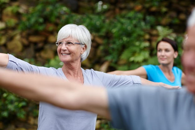 Photo keep calm and do yoga shot of a senior woman doing yoga with other people outdoors