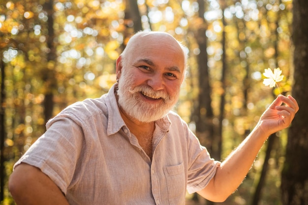 Keep cheerfulness Pensioner hiking in forest on sunny autumn day See beauty in simple things Old bearded man collect leaves Happy man enjoy autumn nature Bearded grandfather relaxing in forest