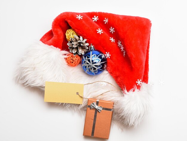 家族の伝統を守ります。サンタさんからのクリスマスプレゼント。冬休みの属性。新年とクリスマスのお祝い。サンタ赤い帽子白い背景の上面図。クリスマスのギフトボックスとサンタの帽子。
