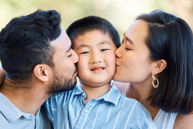 계속해서 키스를 하세요. 정원에서 부모로부터 키스를 받고 있는 사랑스러운 어린 소년의 샷.