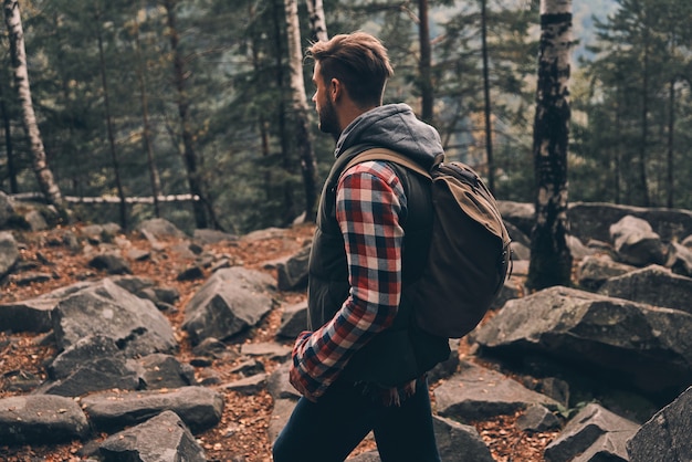 Photo keep moving! young man carrying backpack and looking away while standing in the woods