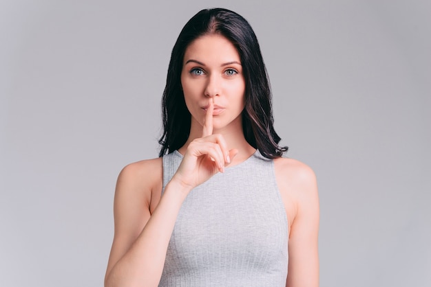 私の秘密を守ってください！立っている間唇に指を保持している魅力的な若い女性