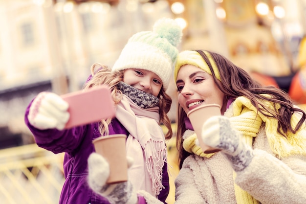 Keep smiling. Charming brunette woman looking at telephone and sitting near her daughter