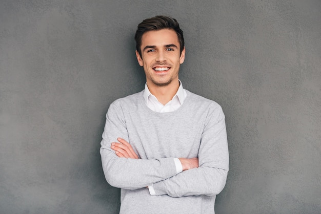 Keep smiling. Confident young man keeping arms crossed with smile while standing 