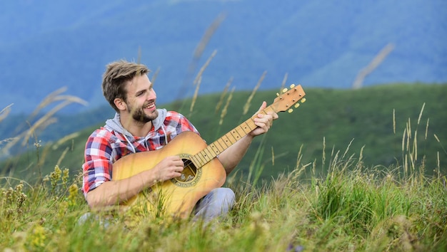 Keep a song in your heart sexy man with guitar in checkered\
shirt hipster fashion western camping and hiking happy and free\
cowboy man with acoustic guitar player country music song