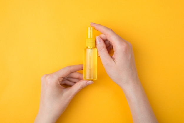 Photo keeping germs away from hands concept. top above overhead close-up view photo of woman holding a bottle of spray hand sanitizer isolated on yellow color bright background