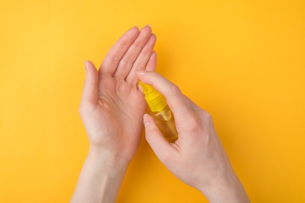 Foto mantenere le mani pulite concetto. vista ravvicinata dall'alto sopra la foto di una donna che usa un disinfettante per le mani spray isolato su sfondo giallo