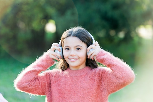 彼女の娯楽とのつながりを維持します。屋外の愛らしい少女。彼女が聞きたいのは音楽だけです。ヘッドフォンを身に着けている小さな女の子の子供。幸せな子供は外出先で音楽を聴いて楽しんでいます。