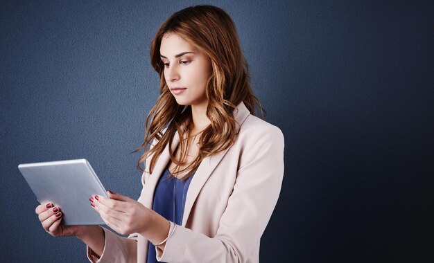 Keeping tabs on business wherever whenever Studio shot of an attractive young businesswoman using a digital tablet against a dark blue background