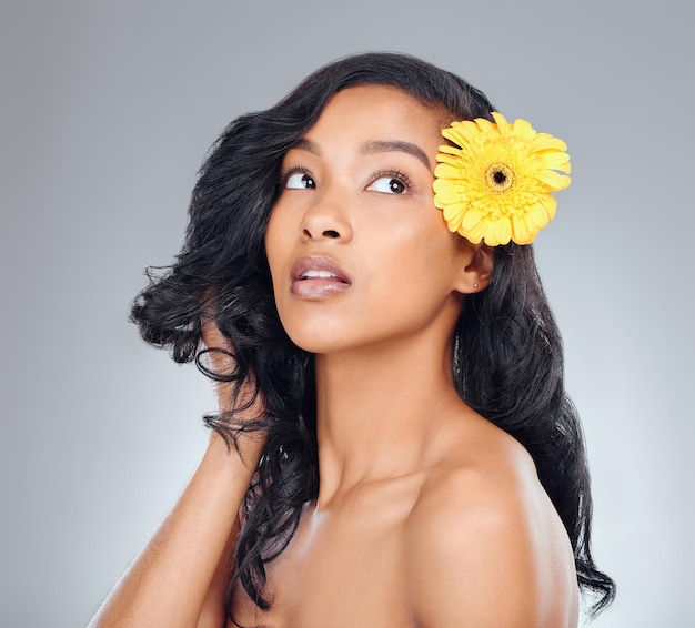 Keeping those bad hair days to a minimal. Studio shot of an attractive young woman posing with a yellow flower in her hair against a grey background.