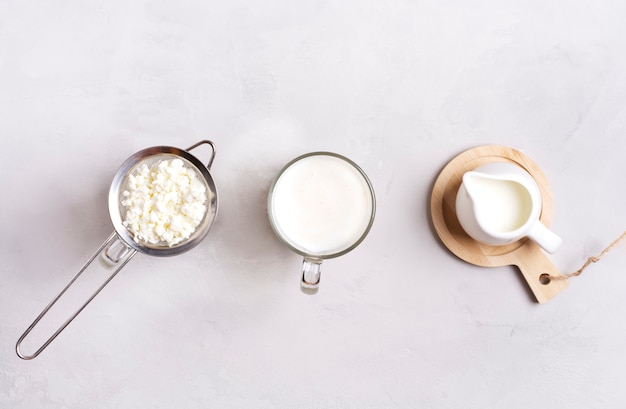 Kefir in a glass, next to kefir grains and milk on a gray surface